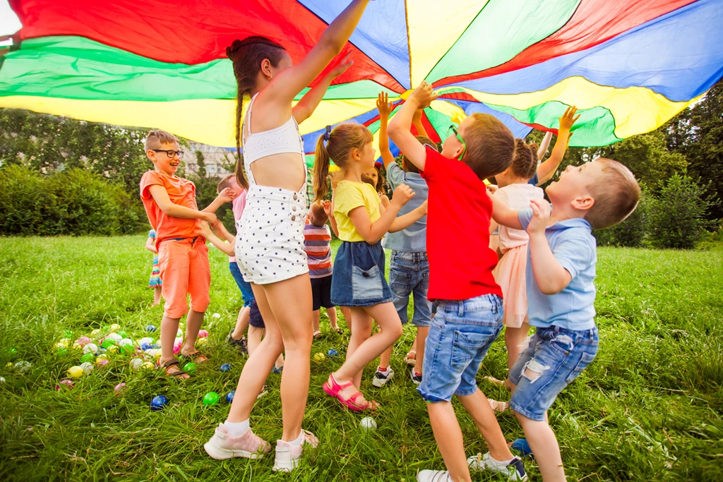 Children make a round under a multicolored canvas in the grass