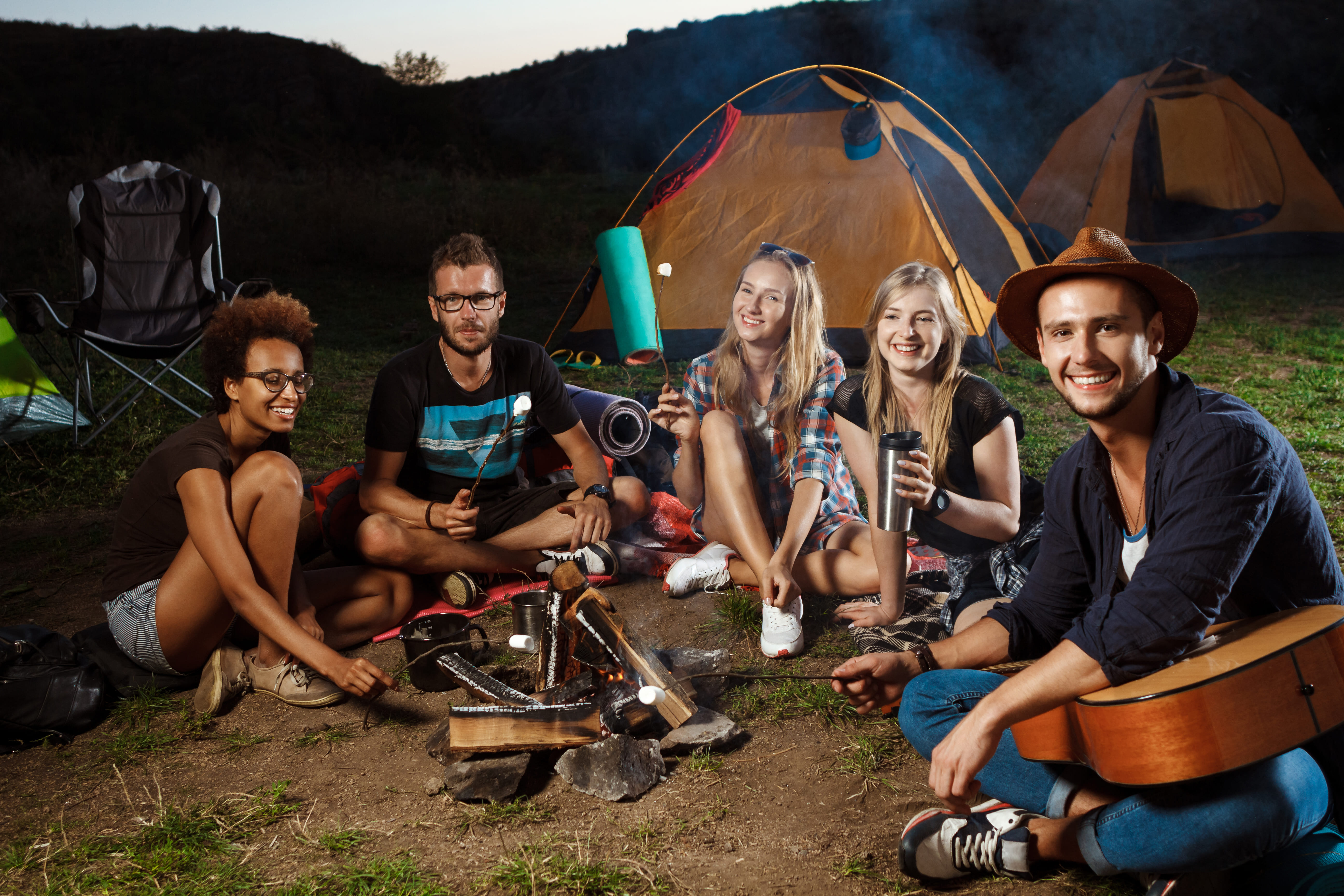 amis assis pres de feu de joie souriant jouant de la guitare camping grill guimauve (1)